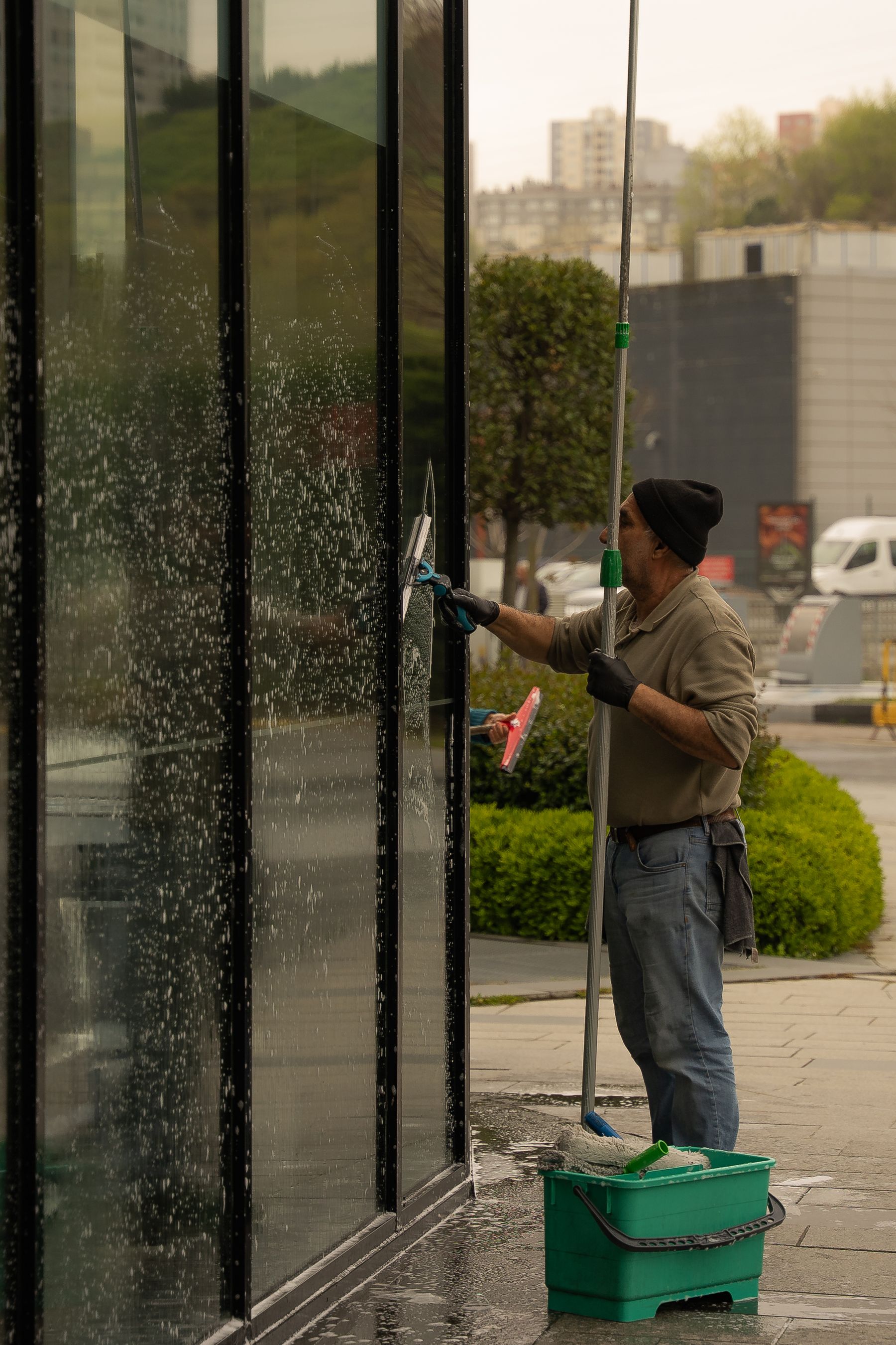 Vinduespudser arbejder med skraber og teleskopstang på en glasfacade